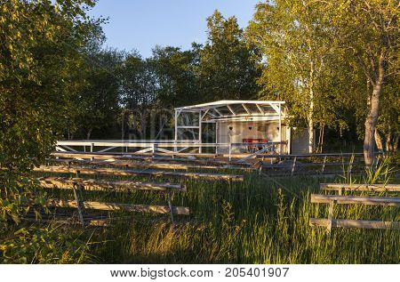 Outdoor, old wooden dance floor in the countryside. Seats and some red cabin, shelter.