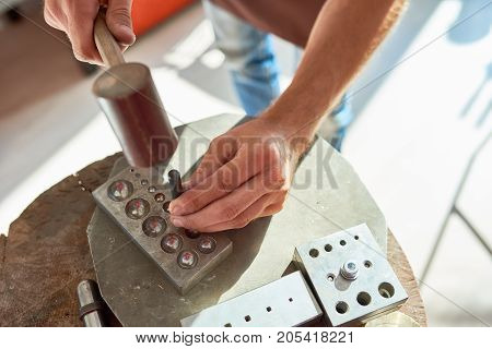 Top view closeup  of young man working with metal in  workshop, forming it with mallet hammer on work station with different tools