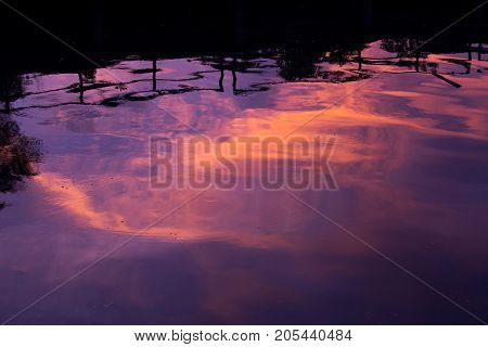 Reflection of clouds and sky in riverin twilight with shadow of rail