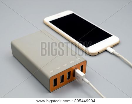 Close-up image of smart phone charging with multiport USB power adaptor on gray background Selective focus