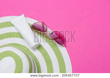 Straw hat and sun block lotion tube and sunglasses on a pink background