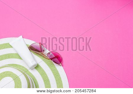 Straw hat and sun block lotion tube and sunglasses on a pink background