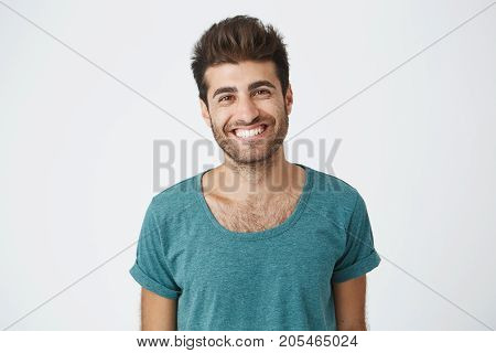 Positive and joyful spanish man with beard wearing blue t-shirt brightly smiling in camera feeling happy about day off on work. People and emotions concept.