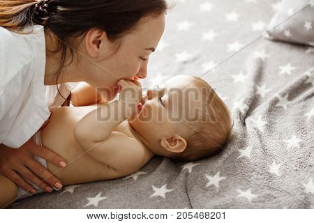 Close up of happy good looking mother playing with her newborn son, kissing and gently biting his little hands. Happy motherhood concept