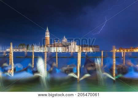 San Giorgio Maggiore church and gondolas in Venice, Italy during blue hour with dramatic sky and lighting. Focus on the church