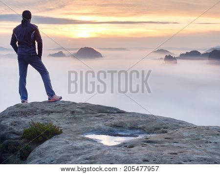 Man stands alone on the peak of rock. Hiker watching to autumn Sun at horizon . Beautiful moment the miracle of nature. Colorful mist in valley. Man hike. Person silhouette stand