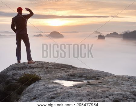 Man stands alone on the peak of rock. Hiker watching to autumn Sun at horizon . Beautiful moment the miracle of nature. Colorful mist in valley. Man hike. Person silhouette stand