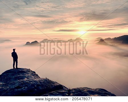 Man stands alone on the peak of rock. Hiker watching to autumn Sun at horizon . Beautiful moment the miracle of nature. Colorful mist in valley. Man hike. Person silhouette stand