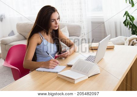 Beautiful brunette woman overwrites information from internet to her notebook. Education woman learn a new information.