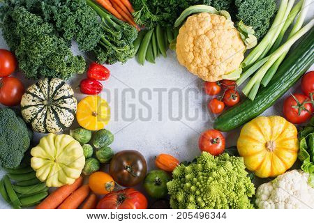 Rainbow colour vegetables arranged in a circle on the light grey background, copy space for text in the middle, top view selective focus