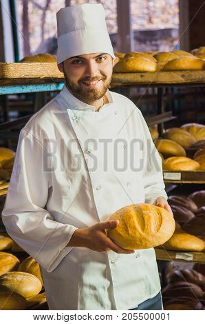 Baker. A Young Handsome Baker Working On A Bread Background Holding Bread In His Hands. Industrial P
