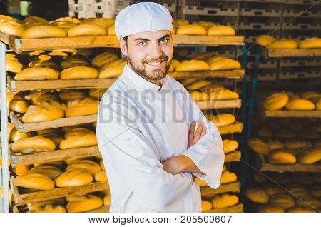 Baker. Bakery. A Young Handsome Worker At A Bakery On The Background Of A Rack With Ready-made Bread