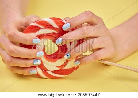 Feminine hands holding bright lollipop. Female hands with stylish winter design nails holding lollipop close up.