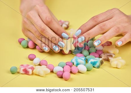 Colorful candies in womans hands. Womans hands with bright manicure taking a colorful candy, yellow background.