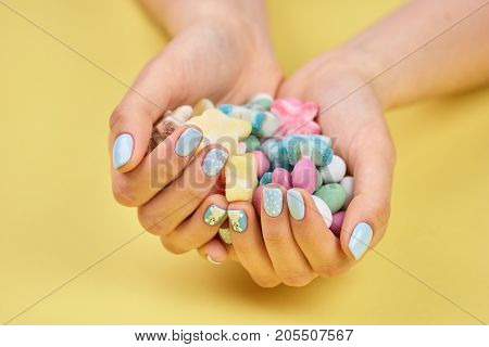 Colorful candies in womans hands. Young woman manicured hands holding colorful candies, yellow background.