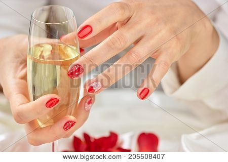 Female manicured hands with champagne. Woman hands with beautiful romantic design manicure holding glass of champagne.