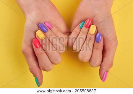 Female nails varnished in different colors. Womans nails covered with multicolor polish on yellow background, top view.