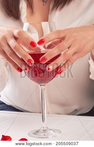 Wine glass in female manicured hands. Woman hands with red polish holding large glass with wine. Young woman hands with glass of wine.