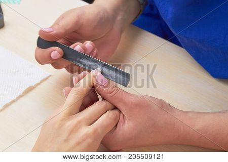 Beautician filing nails to client. Woman hands in nail salon receiving manicure. Young woman is getting manicure in a beauty salon.