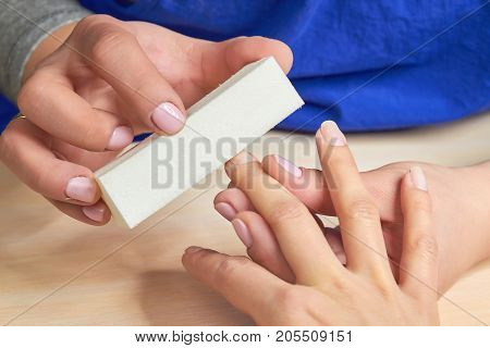 Manicurist polishing nails to client. Beautician filing nails for clients with buffing. Close up of female hands having manicure.