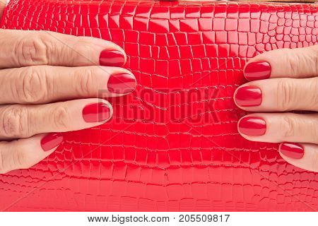 Close up red leather purse in female hands. Woman hands with red manicure holding red lacquered handbag close up.