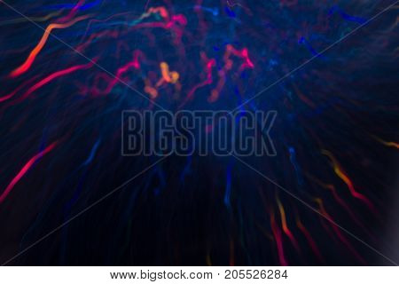 Abstract background of colorful crankles in motion on black. Bokeh of defocused curves, blurred neon blue, orange and purple leds, festive backdrop of fireworks, holidays and celebrations