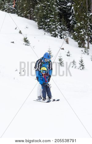 Young child going up a hill with a surface lift together with his father using one button ski lift. Little skier learning in winter school in an Austrian resort