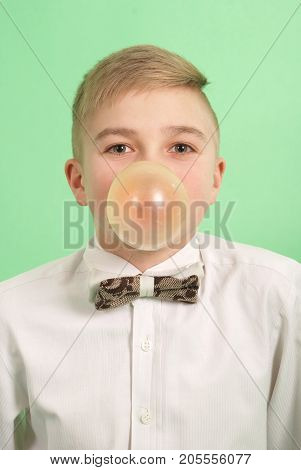 Boy blowing a bubblegum bubble isolated on green