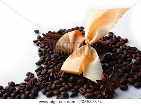 White background roasted coffee beans star anise cinnamone sticks with orange ribbon bow. Oriental recipe for making coffee.