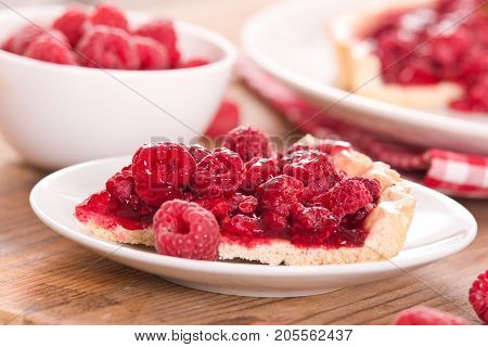 Raspberry tart with fresh rasperries in white bowl.
