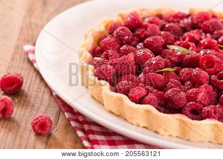 Raspberry tart with fresh rasperries in white bowl.