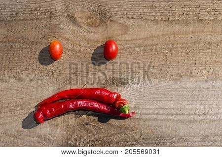 hili and tomatoes on an old wooden board, laid out in the form of an emoticon