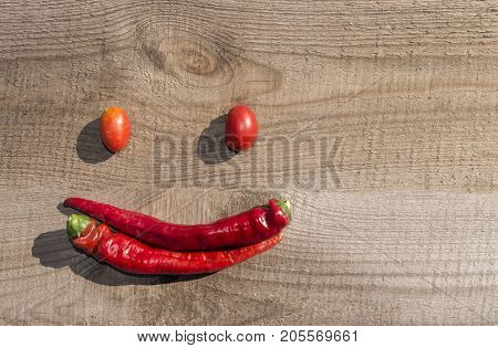 hili and tomatoes on an old wooden board, laid out in the form of an emoticon