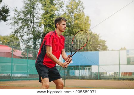 Handsome man in shirt holding tennis racket and looking concentrated while standing on tennis court. Outdoot. Copy-space