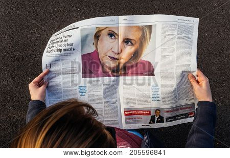 PARIS; FRANCE - SEP 24; 2017: View from above of woman reading latest newspaper Le Monde with portrait of Hillary Clinton article about how Donald Trum has lost the moral leadership of United States