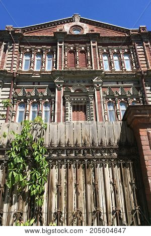 The old red brick house with a high fence on sky background