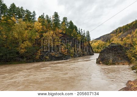 Beautiful Kamchatka autumn landscape: mountain river flowing among roky mountain through the colorful forest. Eurasia Russian Far East Kamchatka Peninsula.