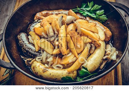 Fried sausages with baked potatoes, in a frying pan. Top view.