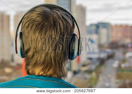 The guy in the headphones stands with his back against the backdrop of the city, listens to music as a music lover.