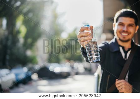 bottle of pure mineral water in the hand of a young happy man. Autumn street day.