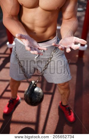 A strong man with sexy body is doing exercises on his feet. A handsome young man lifts weights with his feet in the park.