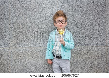 Fashion baby boy in mint jacket stands on a gray wall background. Trendy boy with lollipop standing on the street.