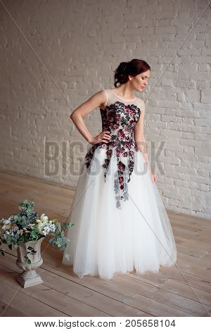 Beautiful luxurious female model with medium brown hair in a long fashinable dress standing in the room. Bridal clothes concept. Stylish wedding dress.