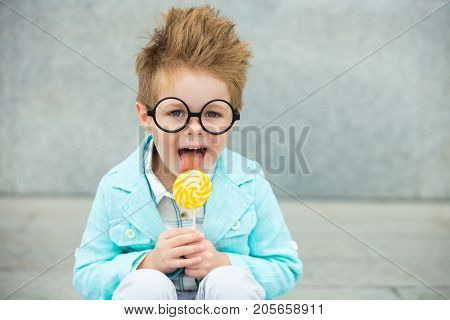 Fashion baby boy in mint jacket stands on a gray wall background. Trendy boy with lollipop standing on the street.