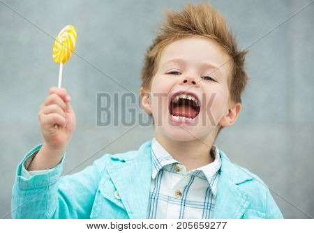 Fashion baby boy in mint jacket and sneakers stands on a gray wall background. Trendy boy with lollipop standing on the street.