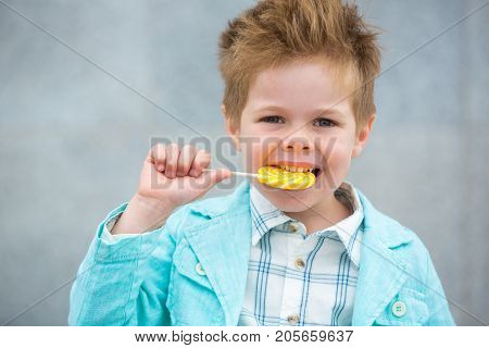 Fashion baby boy in mint jacket and sneakers stands on a gray wall background. Trendy boy with lollipop standing on the street.