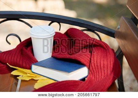 A glass of teaa is on a brown table with a warm scarf and an interesting book Close-up of equipment.