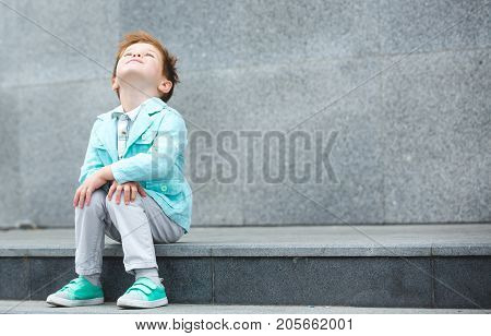 Fashion baby boy in mint jacket and sneakers posing on a gray wall background. Trendy boy standing on the street.
