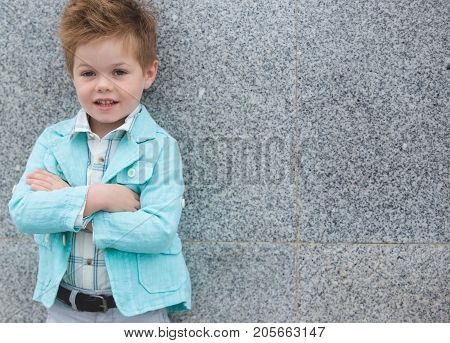 Fashion baby boy in mint jacket posing on a gray wall background. Trendy boy standing on the street.