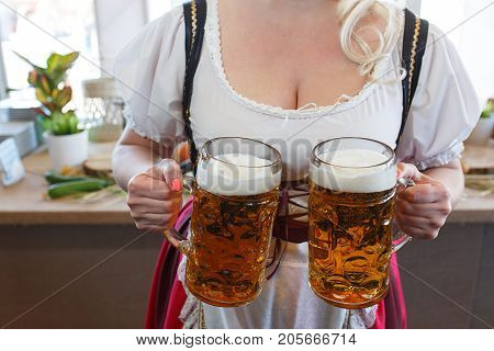 Girl in a traditional dress with a big breasts and deep neckline holds full mugs of beer during the celebration of the Oktoberfest